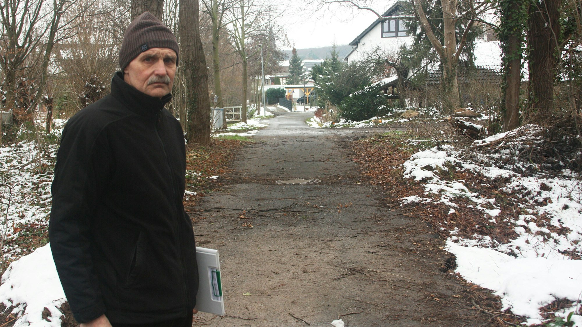 Blindert im Wald bei Schnee, hinter sich ein Weg, der auf den Ort zuführt.
