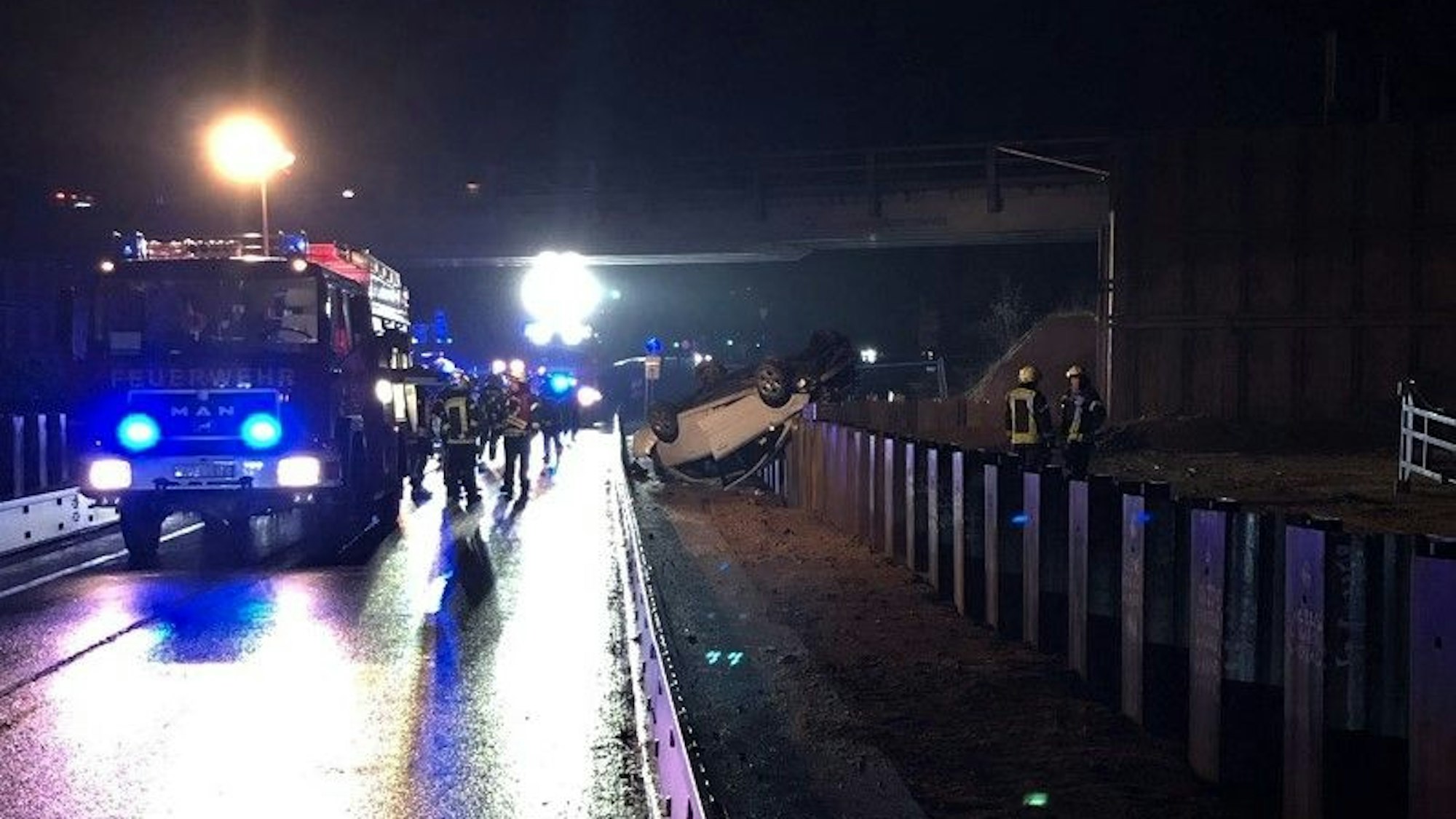 Feuerwehrleute und Polizisten stehen an dem Auto auf der A44, das mutmaßlich wegen gestohlener Warnschilder und Absperrungen von einer demontierten Autobahnbrücke gestürzt ist.