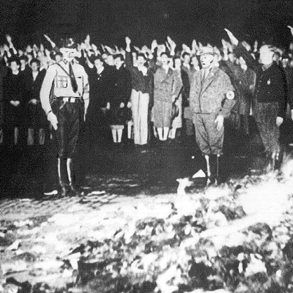 Das Archivbild zeigt eine Bücherverbrennung in Deutschland. Hinter einem brennenden Berg mit Büchern sind Menschen zu sehen, die den Hitlergruß zeigen.
