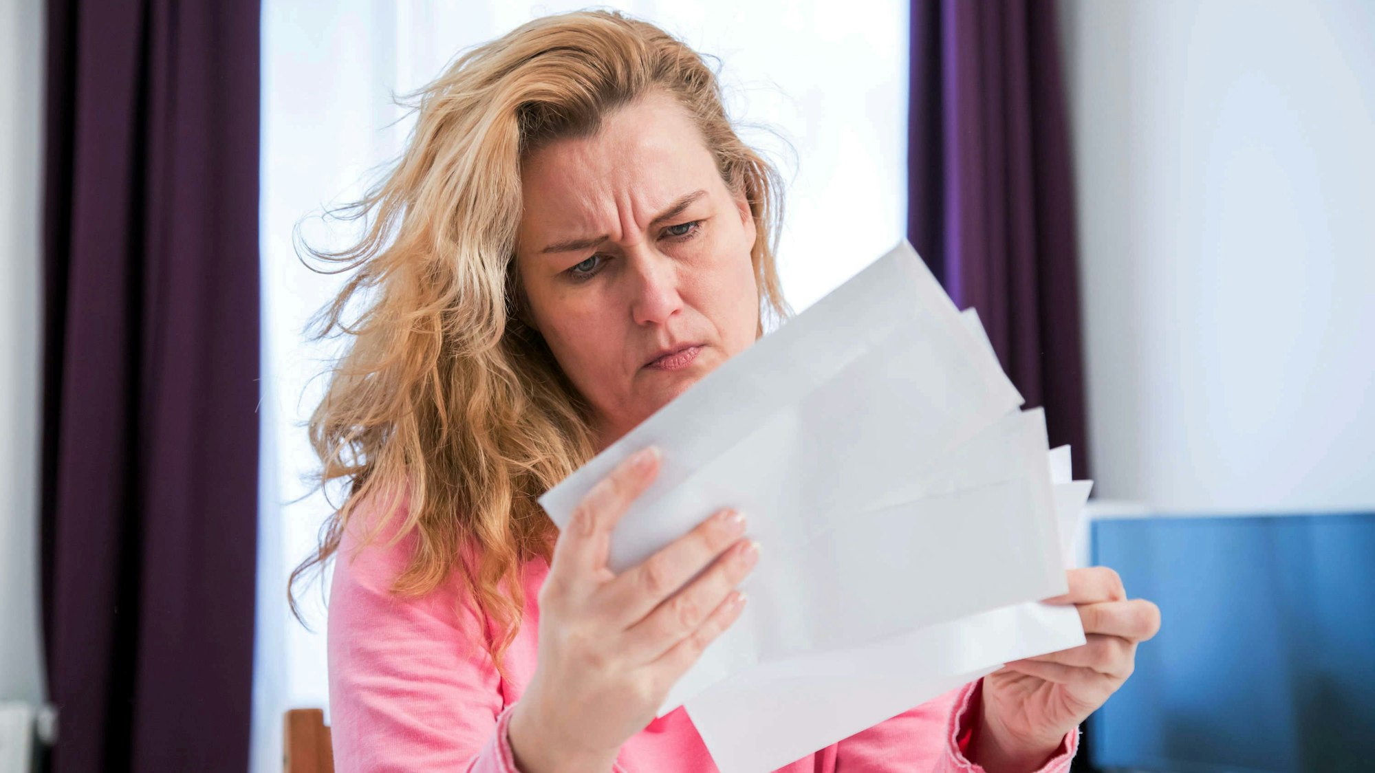 Eine Frau sitzt in ihrer Wohnung und schaut fragend auf einen Brief