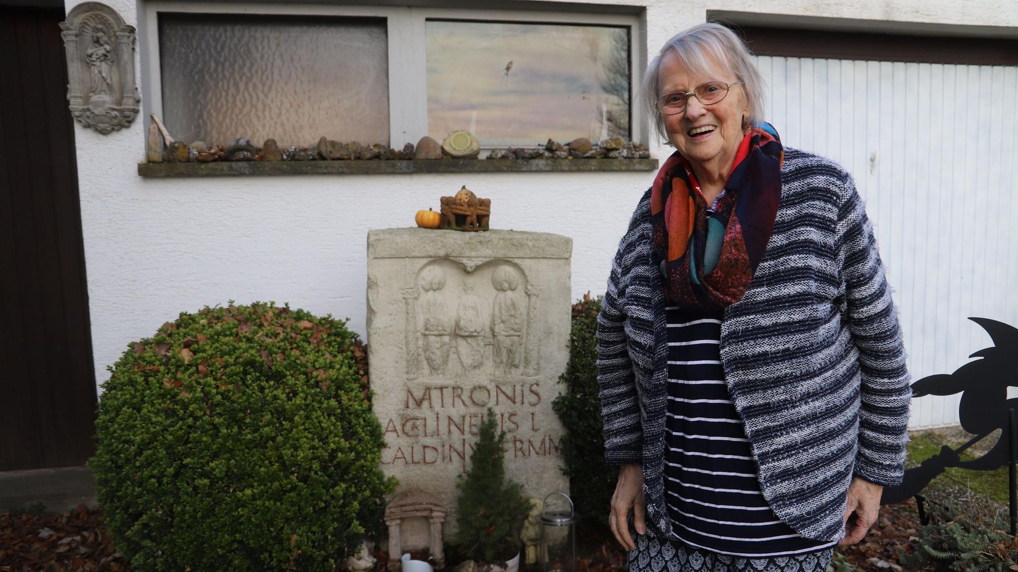 Sophie Lange neben einem Matronen-Stein, hinter ihr ein Haus.