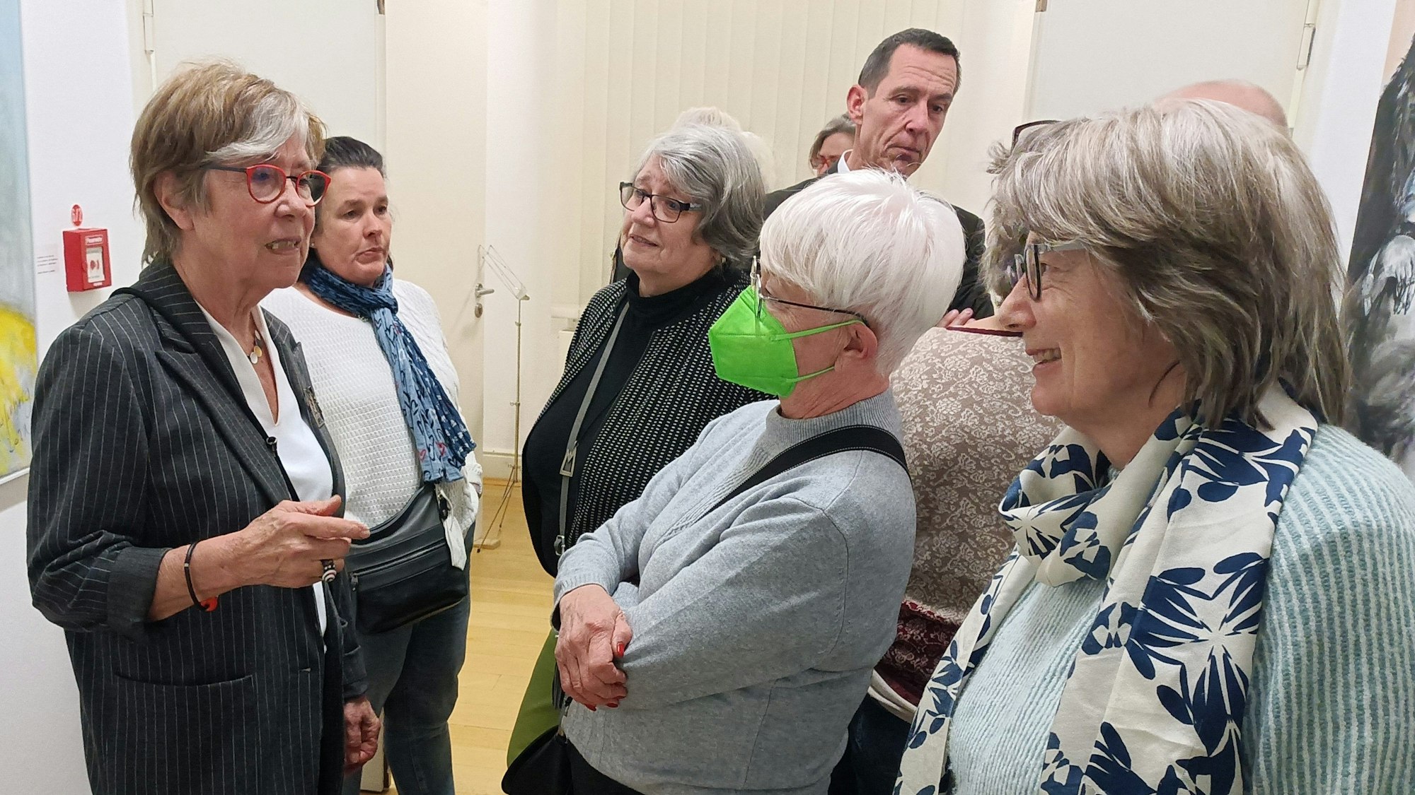 Die Künstlerin Gerda Laufenberg steht links und spricht angeregt mit Besuchern.