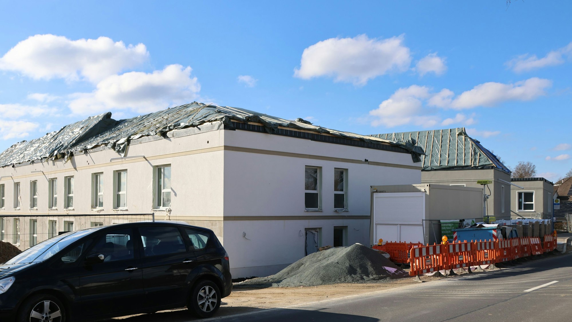 Es ist ein Rohbau zusehen, dessen Dach mit schwarzen Planen abgedeckt ist.