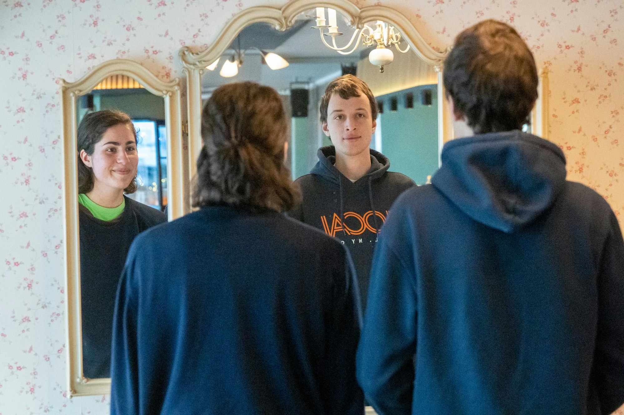 Franka Höfler und Mattes Wiegmann stehen vor einem Spiegel. Ihre Gesichter sind nur im Spiegel zu sehen.