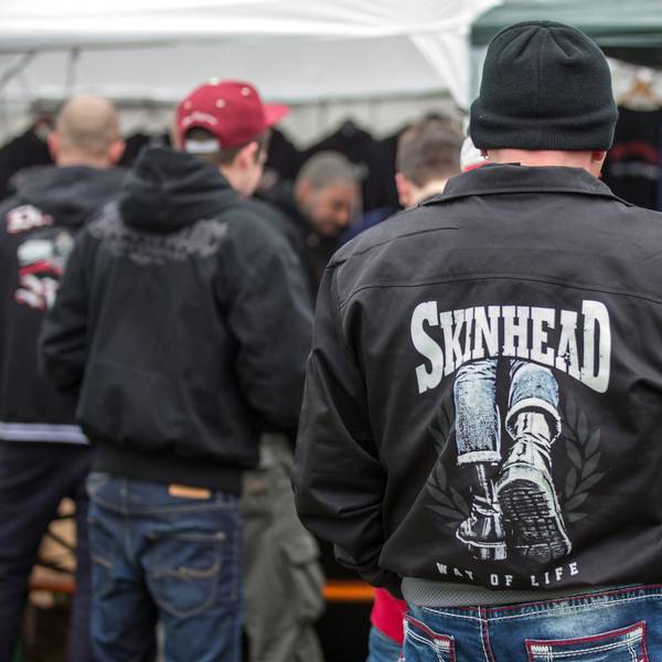 Dunkel gekleidete Personen, oft mit Mützen oder Cappies auf dem Kopf und schwarzen Jacken, teilweise mit Skinhead-Aufdruck.
