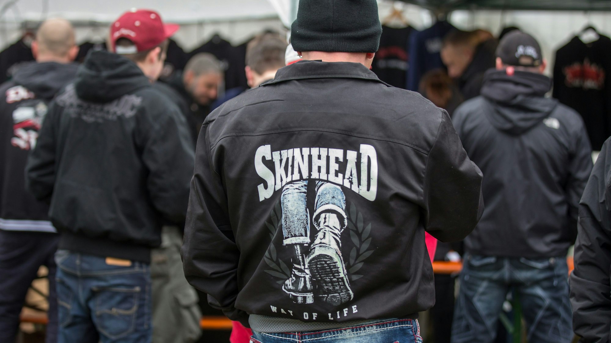 Dunkel gekleidete Personen, oft mit Mützen oder Cappies auf dem Kopf und schwarzen Jacken, teilweise mit Skinhead-Aufdruck.