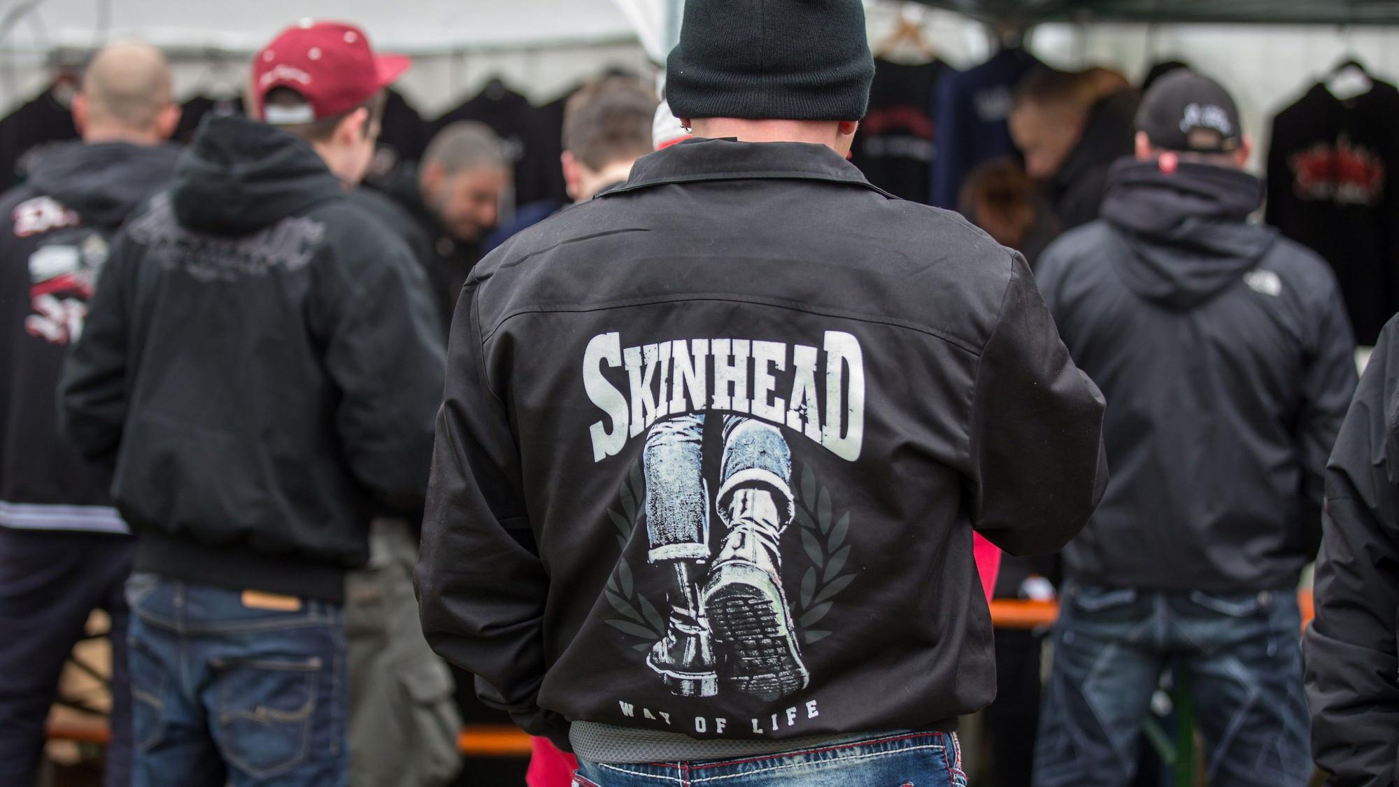 Dunkel gekleidete Personen, oft mit Mützen oder Cappies auf dem Kopf und schwarzen Jacken, teilweise mit Skinhead-Aufdruck.