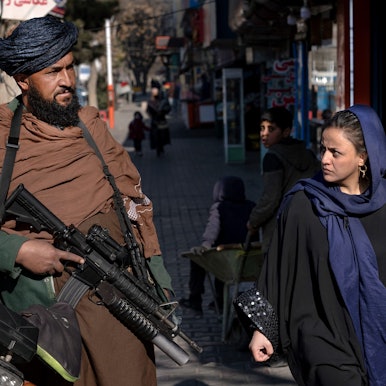 Ein Taliban-Kämpfer steht Wache, während eine Frau vorbeiläuft.