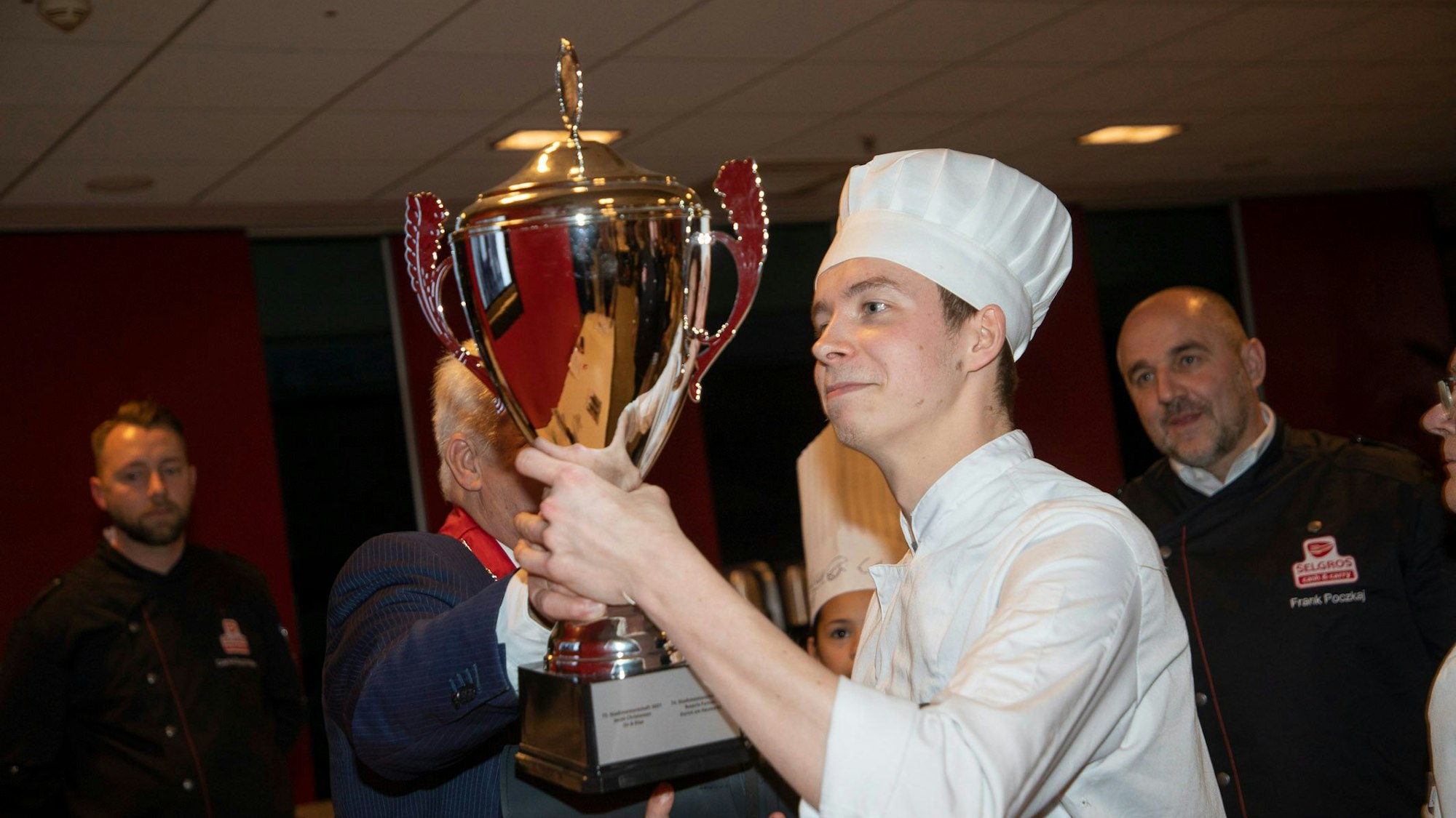Simon Lein hält einen Pokal für den Titel als Kölner Stadtmeister 2023 der Nachwuchsköche in die Höhe.