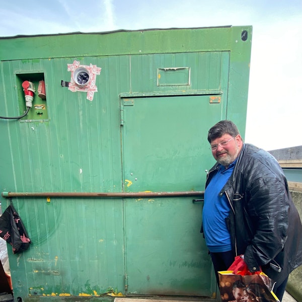 Klaus Berg an der Tür zu seinem Zuhause, er schaut in die Kamera, hinter sich eine grüne Containerwand.