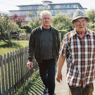 Ivo Batic (Miroslav Nemec, links) und Franz Leitmayr (Udo Wachtveitl, rechts) gehen mit dem Verdächtigen Hackl (Burghart Klaußner) durch eine Kleingartensiedlung. Batic und Leitmeyr schauen ernst, fast genervt. Hackl sieht wütend aus und geht vor ihnen.