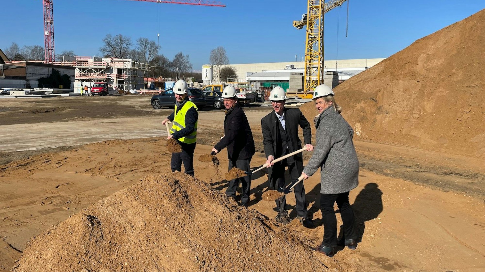 Die vier halten einen Spaten mit Erde in der Hand.