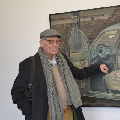 Der Künstler steht vor einem Bild eines Käfers.