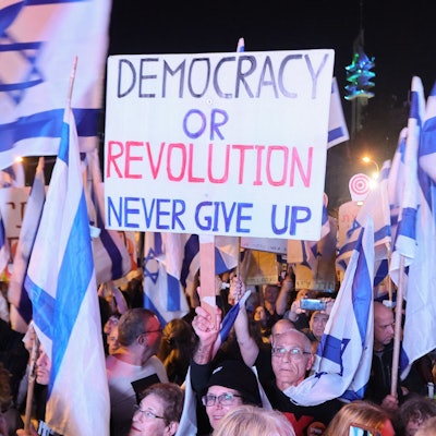 Israelische Bürger demonstrieren in der nordisraelischen Stadt Karmiel gegen die Justizreform ihrer Regierung. Die Demonstrierenden schwenken israelische Flaggen. Auf einem hochgehaltenen Plakat steht: „Democracy or Revolution. Never gib up“ - Demokratie oder Revolution. Niemals aufgeben!