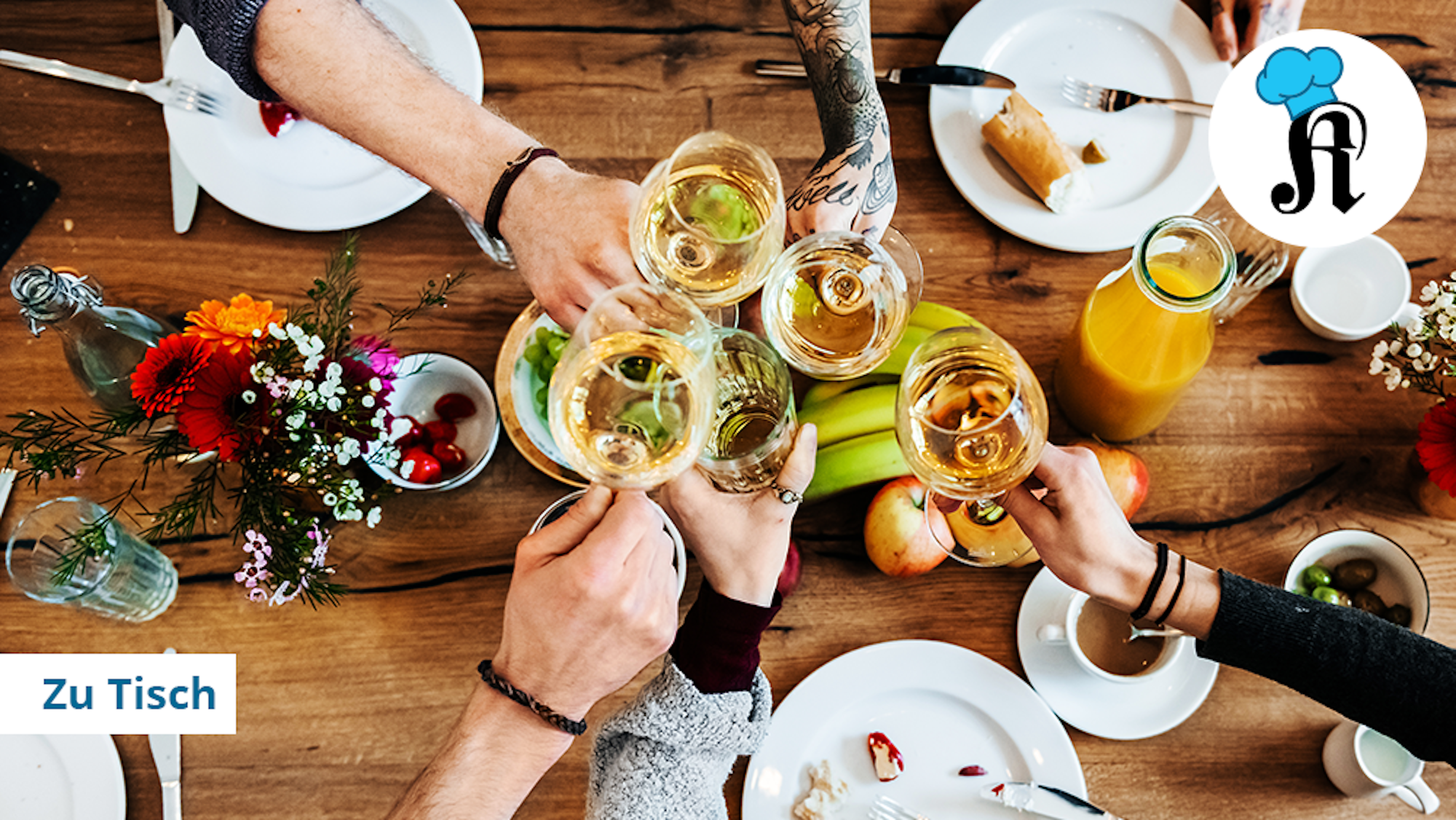 Mehrere Menschen stoßen mit Weingläsern über einem gedeckten Holztisch an.
