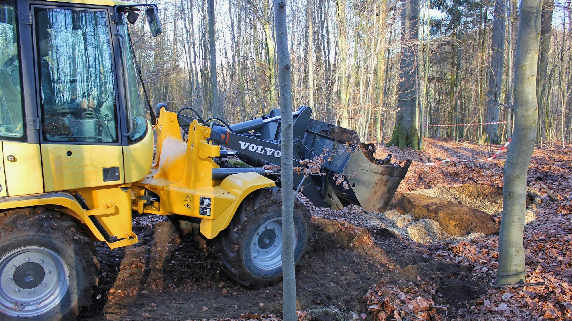 Ein Bagger füllt ein Loch im Waldboden.