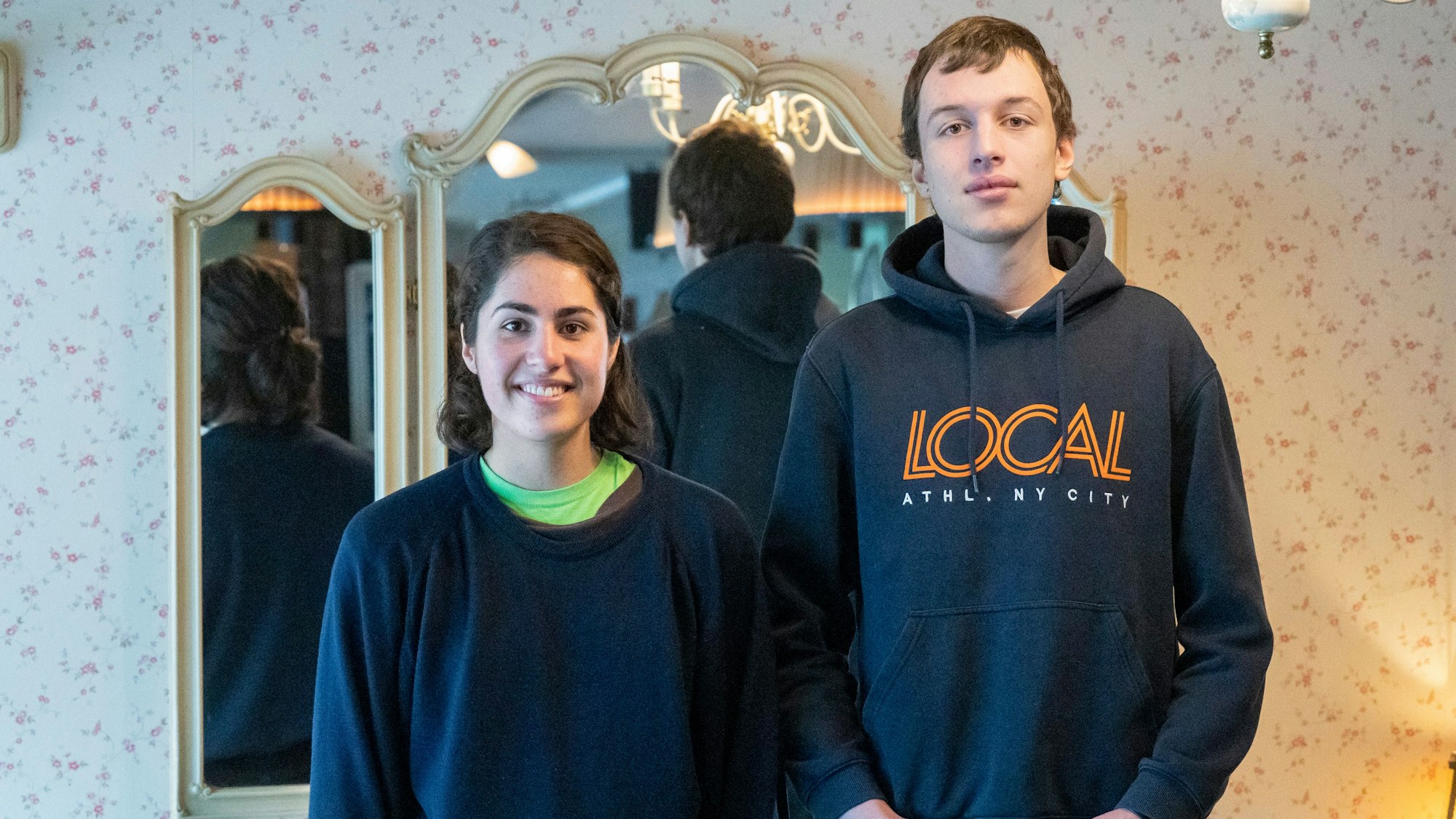 Franka Höfler und Mattes Wiegmann stehen vor einem Spiegel und schauen in die Kamera.