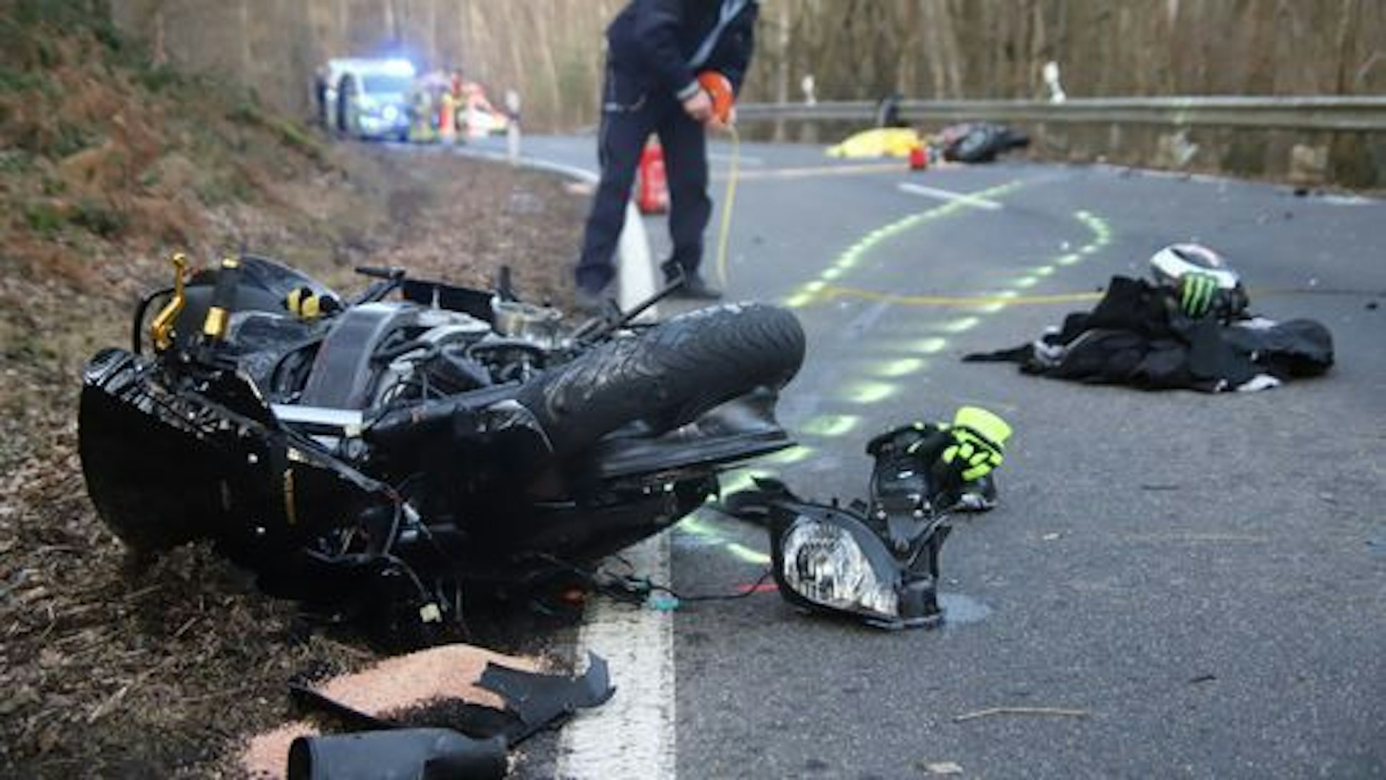 Nach einem Unfall in Much am 20. Februar 2021 liegen Teile eines Motorrads auf der Straße. Ein Polizist sichert die Szene.