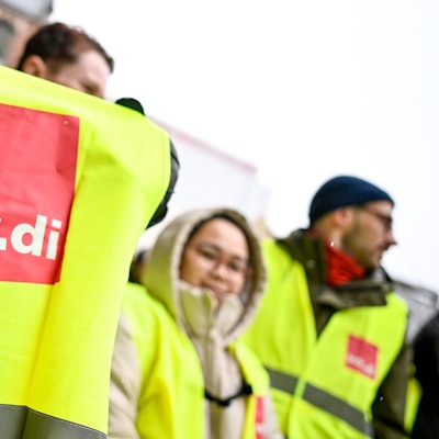 Das Foto zeigt Beschäftigte des Öffentlichen Dienstes in gelben Streikwesten. Im Vordergrund ist das Logo der Gewerkschaft Verdi zu sehen.