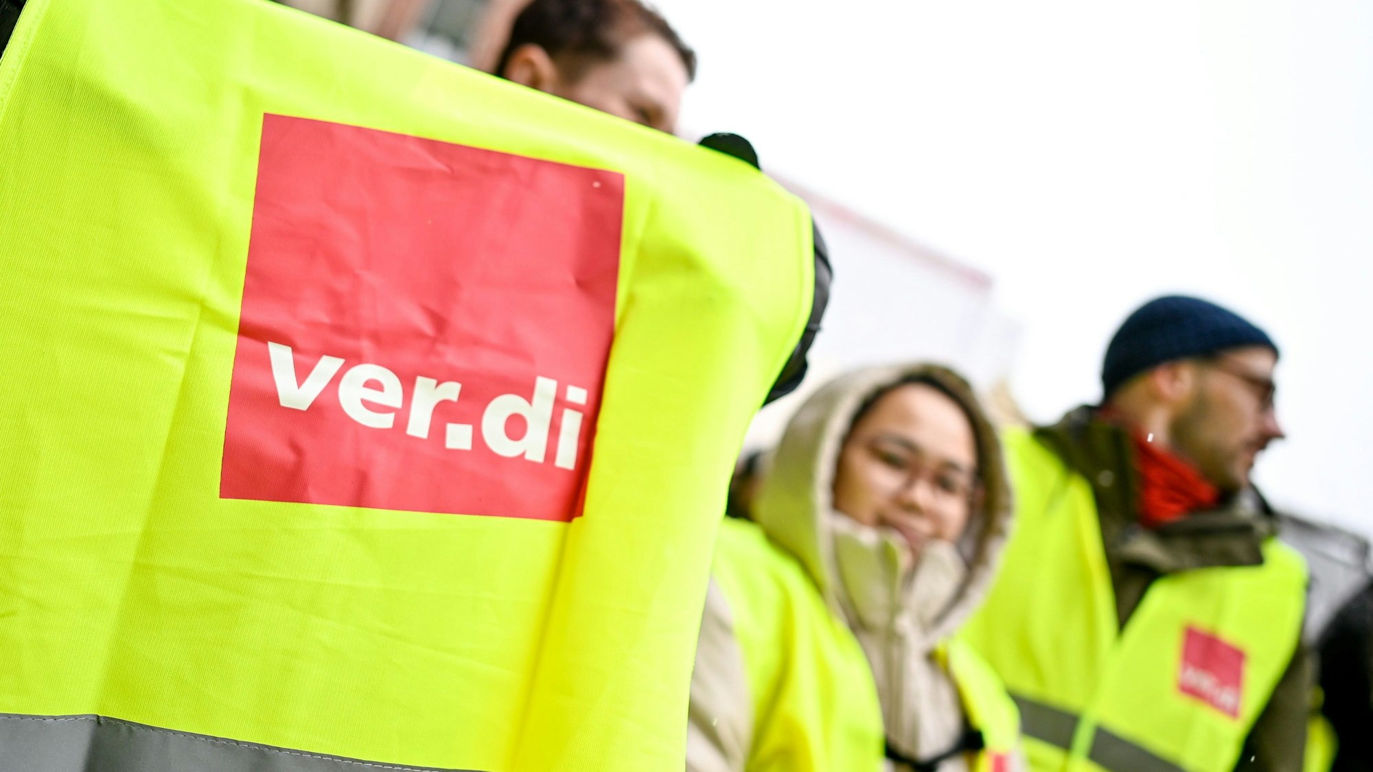 Das Foto zeigt Beschäftigte des Öffentlichen Dienstes in gelben Streikwesten. Im Vordergrund ist das Logo der Gewerkschaft Verdi zu sehen.