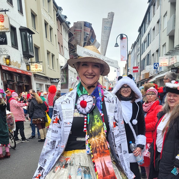 Elke Franke mit einem Hut, der mit Zeitungsseiten geschmückt ist, zwischen Jecken auf der Severinstraße