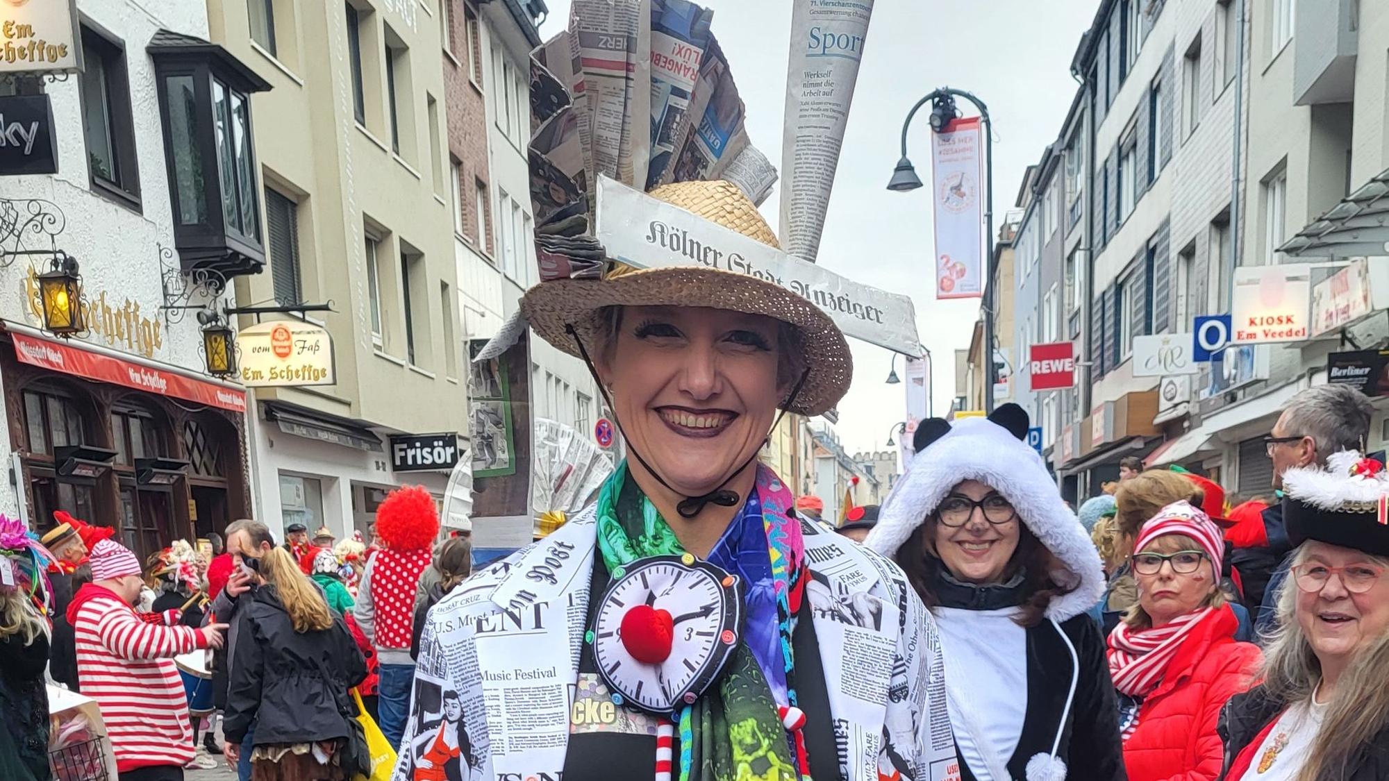 Elke Franke mit einem Hut, der mit Zeitungsseiten geschmückt ist, zwischen Jecken auf der Severinstraße