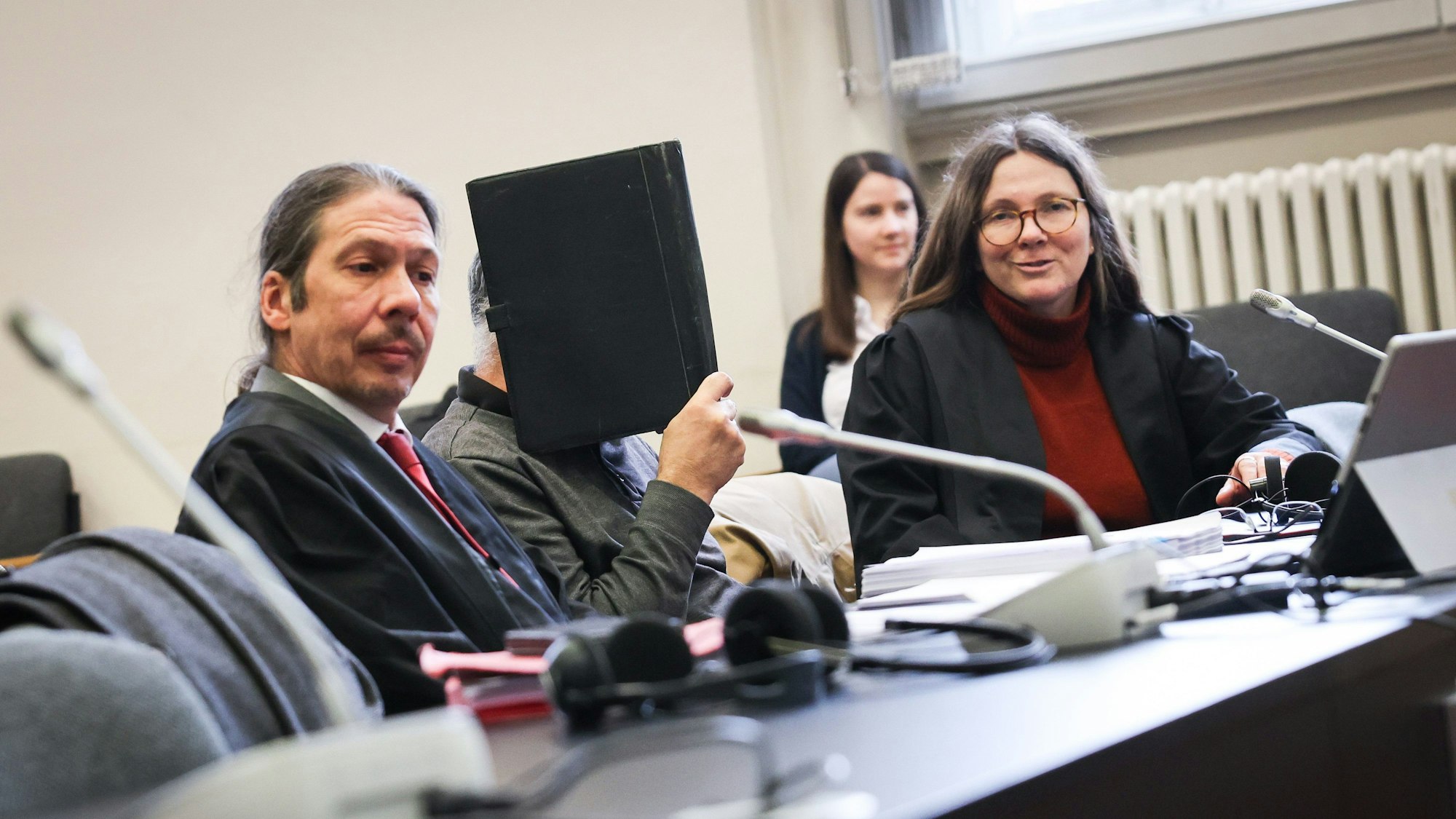 Ein Angeklagter sitzt vor Beginn des Prozesstages zwischen seiner Anwältin (r.) und seinem Anwalt (l.) im Gerichtssaal