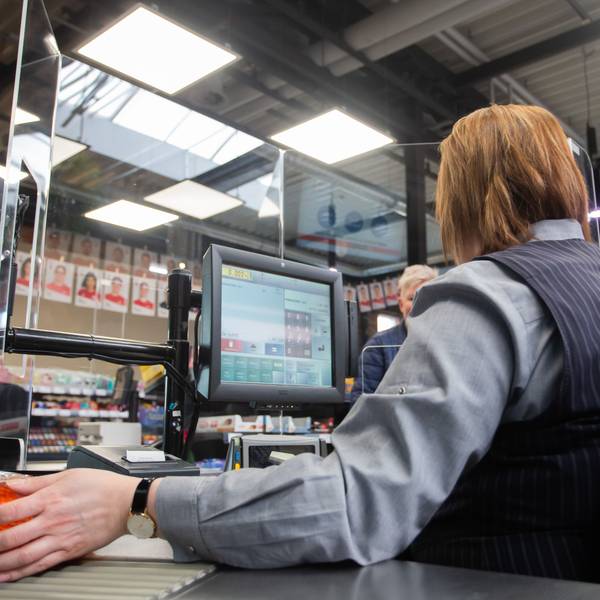 An einer Kasse in einem Supermarkt wird die Kassiererin mit einer Plexiglasscheibe, einem sogenannten "Spuckschutz", geschützt-