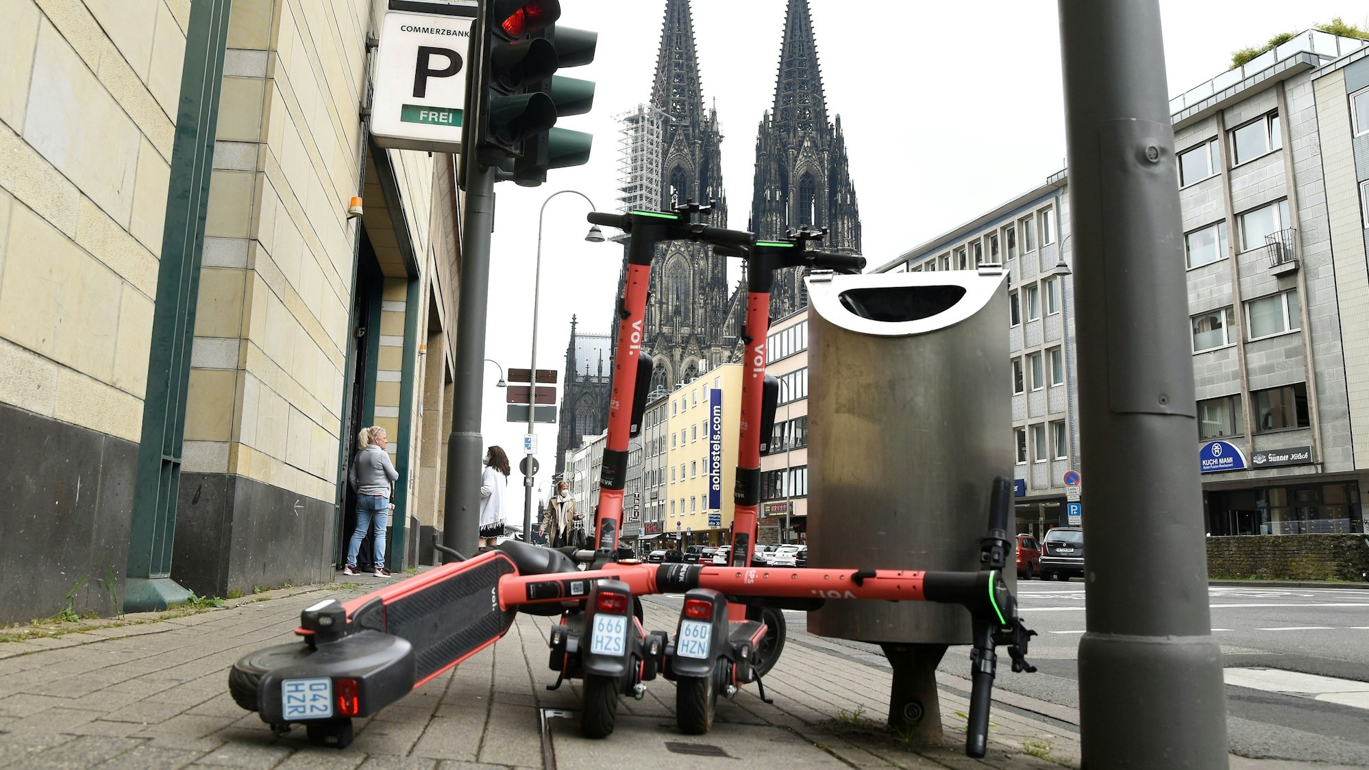 Drei E-Scooter stehen auf dem Bürgersteig. Im Hintergrund ist der Kölner Dom zu sehen.