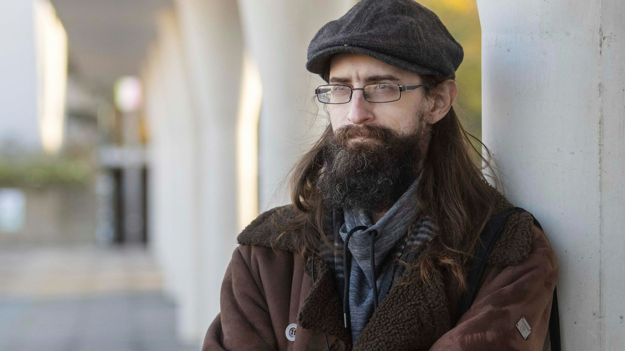 Clemens J. Setz (mit Bart, Brille und Schiebermütze) lehnt an einer Säule.