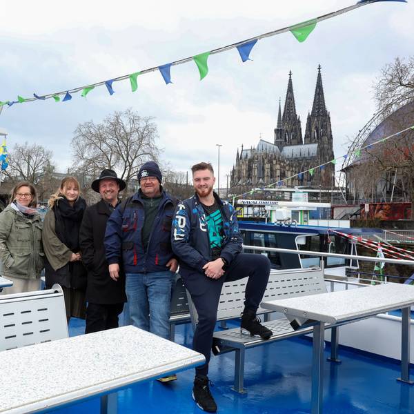 Das Team von Köln-Tourist auf dem Deck eines Schiffes, im Hintergrund der Dom und der Musical Dome