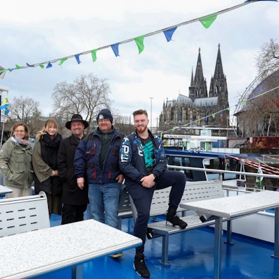 Das Team von Köln-Tourist auf dem Deck eines Schiffes, im Hintergrund der Dom und der Musical Dome