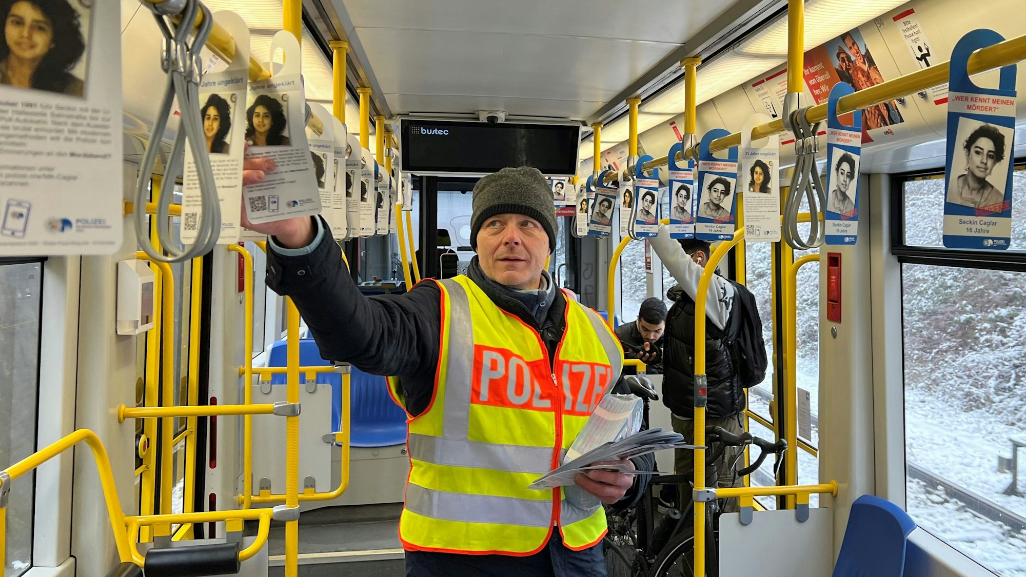 Kriminalhauptkommissar Ulrich Riepelmeier hängt Zettel mit Fahndungsaufrufen zum Cold Case Seckin Caglar in einer KVB-Bahn der Linie 7 auf.