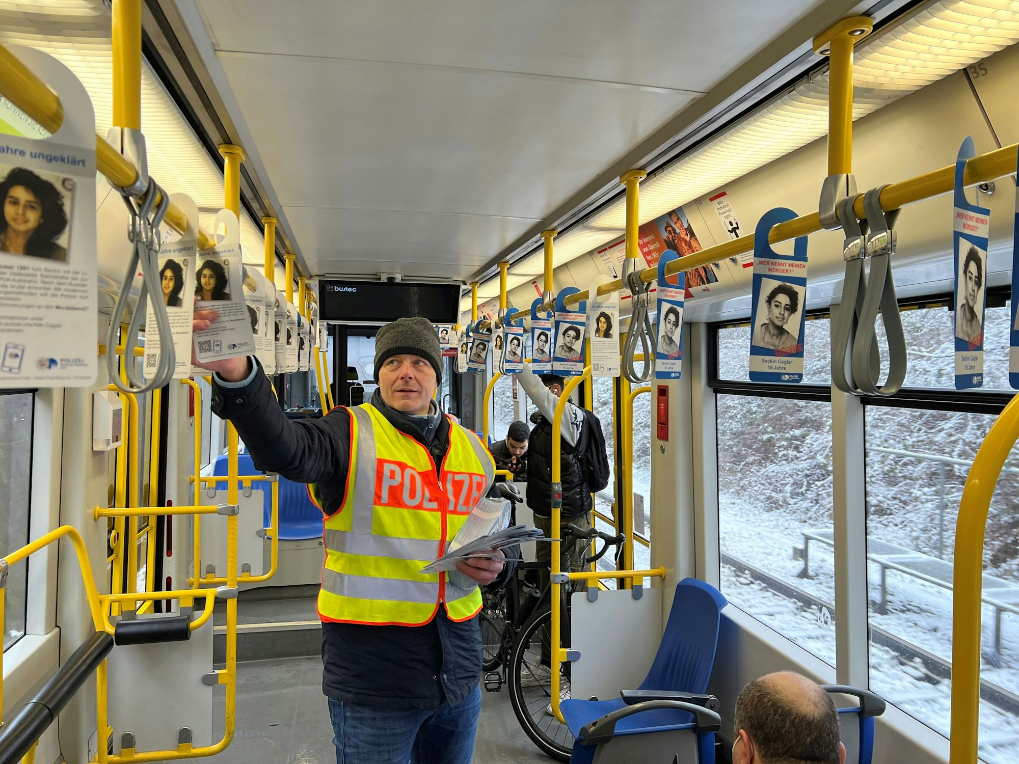 Kriminalhauptkommissar Ulrich Riepelmeier hängt in Poll Fahndungszettel zum Cold Case Seckin Caglar in einer KVB-Bahn der Linie 7 auf.