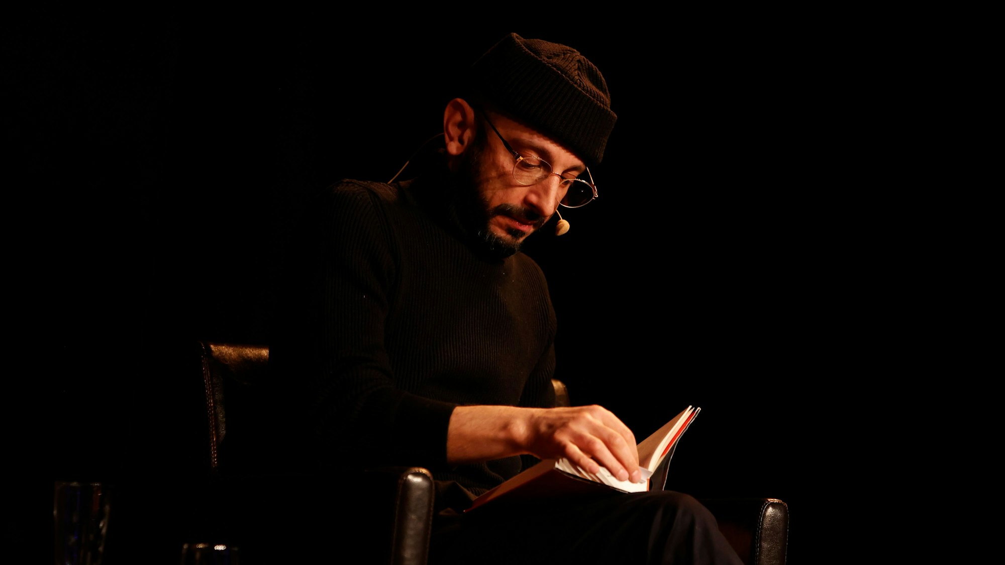 Behzad Karim Khani liest aus seinem Debüt-Roman „Hund, Wolf, Schakal“. Er sitzt auf der Bühne im Literaturhaus, seine Beine sind überschlagen, darauf liegt sein Buch, in dem er gerade eine Seite umblättert. Er schaut ernst aufs Buch hinab.