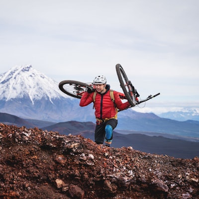 Tobias Woggon trägt sein Mountainbike einen Berg hinauf.