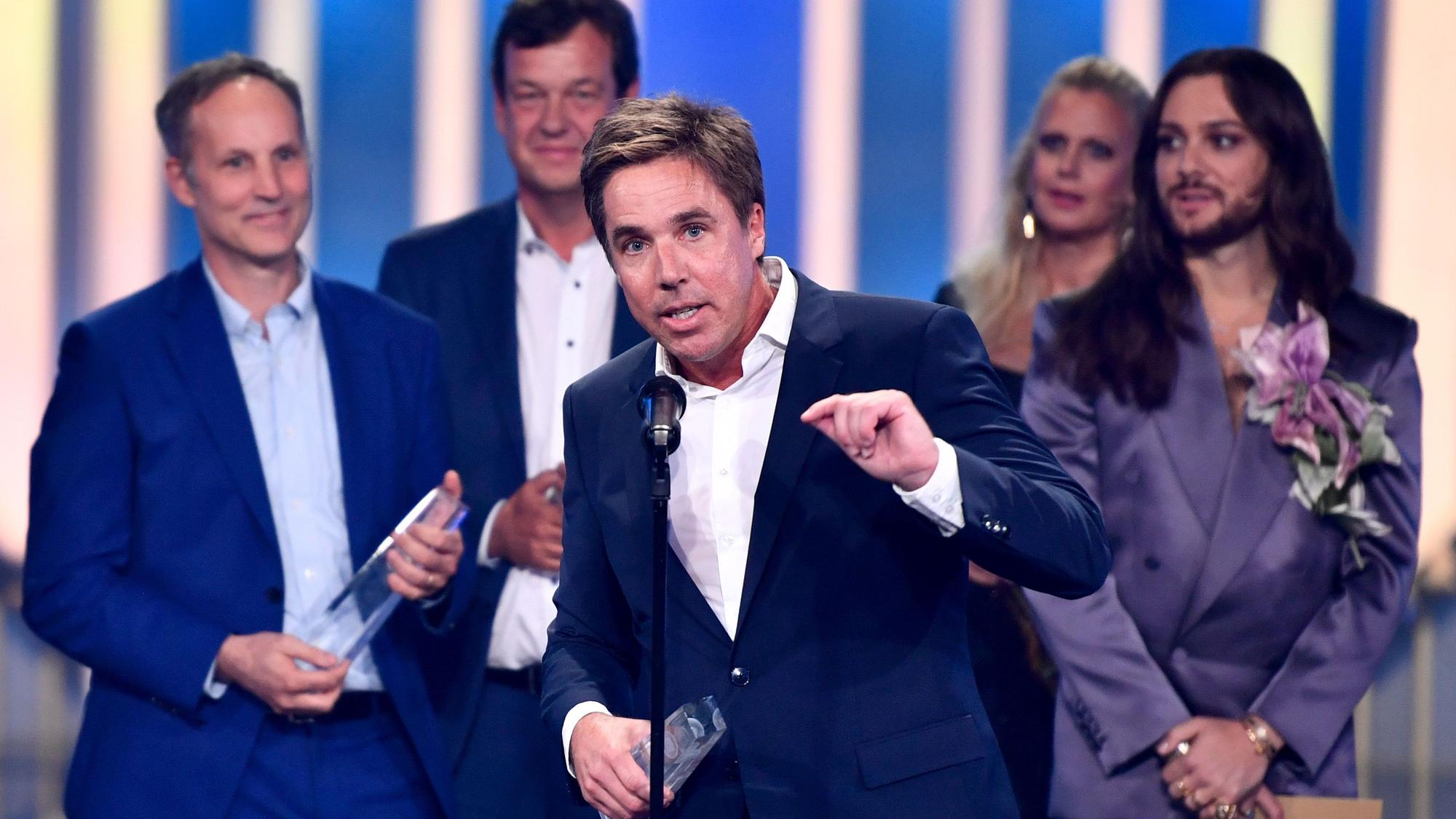 Markus Feldenkirchen spricht in ein Mikro, gestikuliert mit einer Hand und hält in der anderen die Auszeichnung.