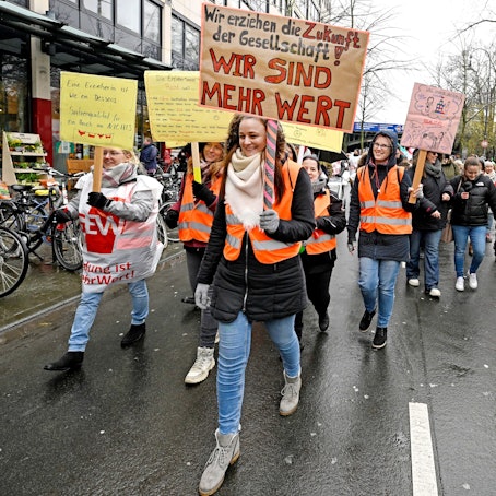 Eine Demonstrantin trägt ein Schild mit der Aufschrift "Wir erziehen die Zukunft der Gesellschaft. Wir sind mehr wert!" auf einer Demo für mehr Lohn in Sozialberufen in Köln.