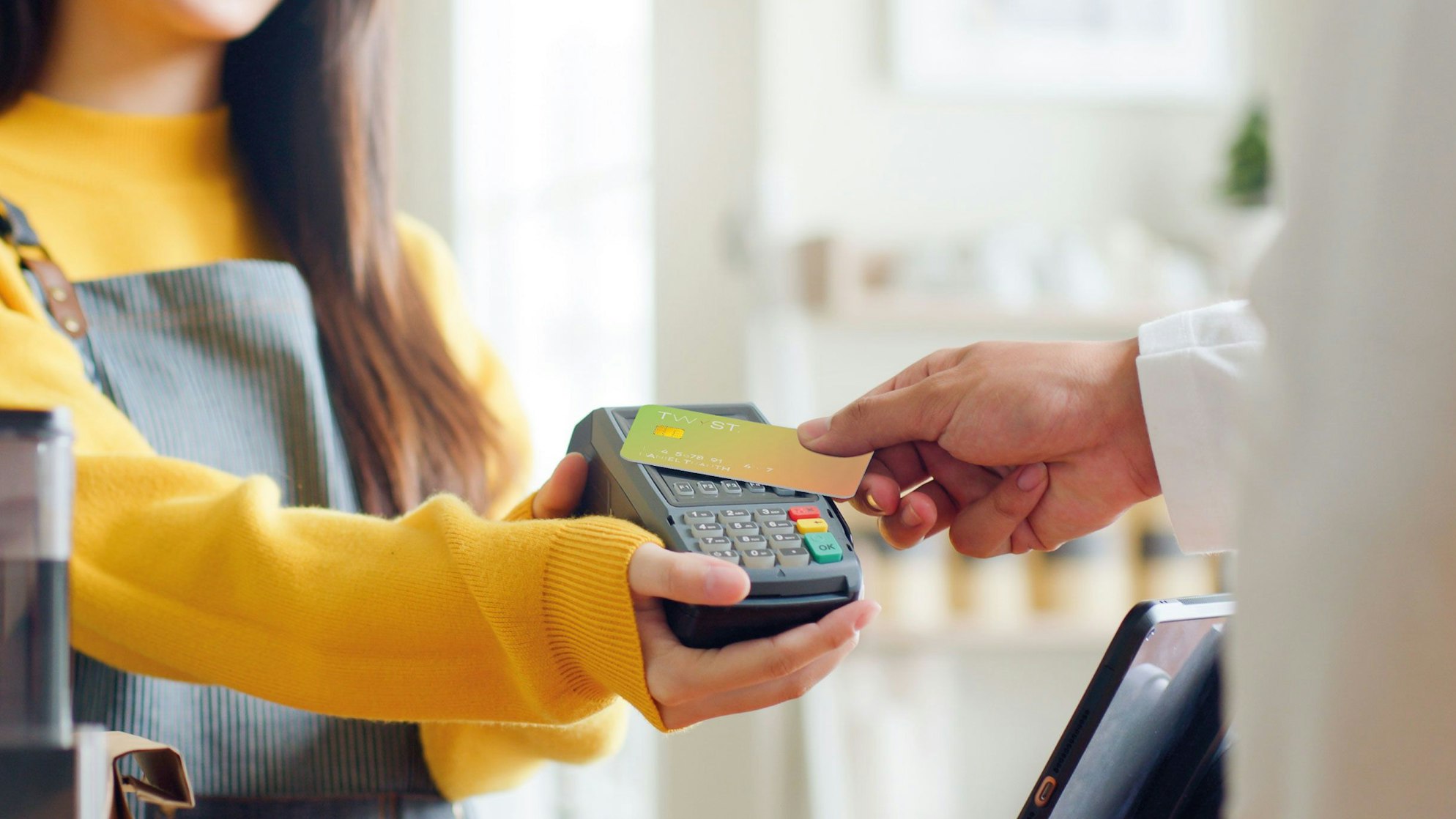 Eine Frau hält das Kartengerät und ein Mann zahlt mit seiner Karte.