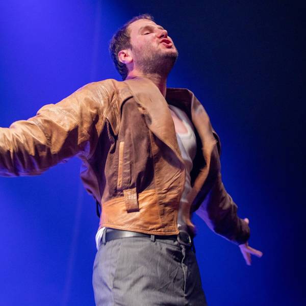 Sänger Marco Michael Wanda von der Band Wanda im Konzert in der Innsbrucker Olympiahalle im Juni 2022. Er hat die Arme aus- und die Brust vorgestreckt und trägt seine abgewetzte braune Lederjacke.