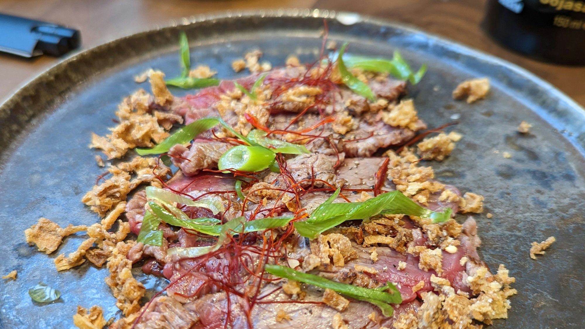 Dünne Streifen aus Rinderfilet liegen auf dem Teller, dazu Röstzwiebeln.
