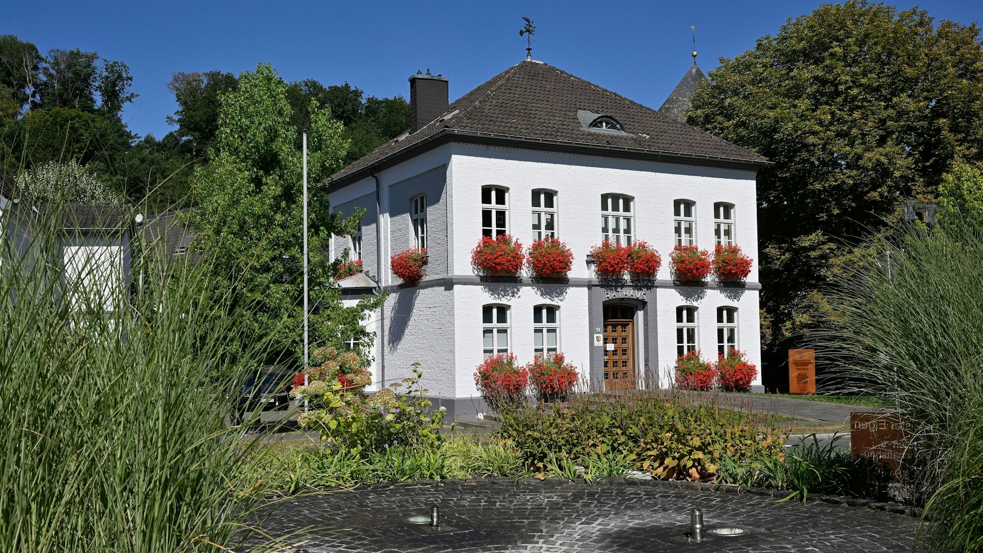 Rathaus Odenthal mit roten Geranien vor den Fenstern, vor dem Haus ein Springbrunnen