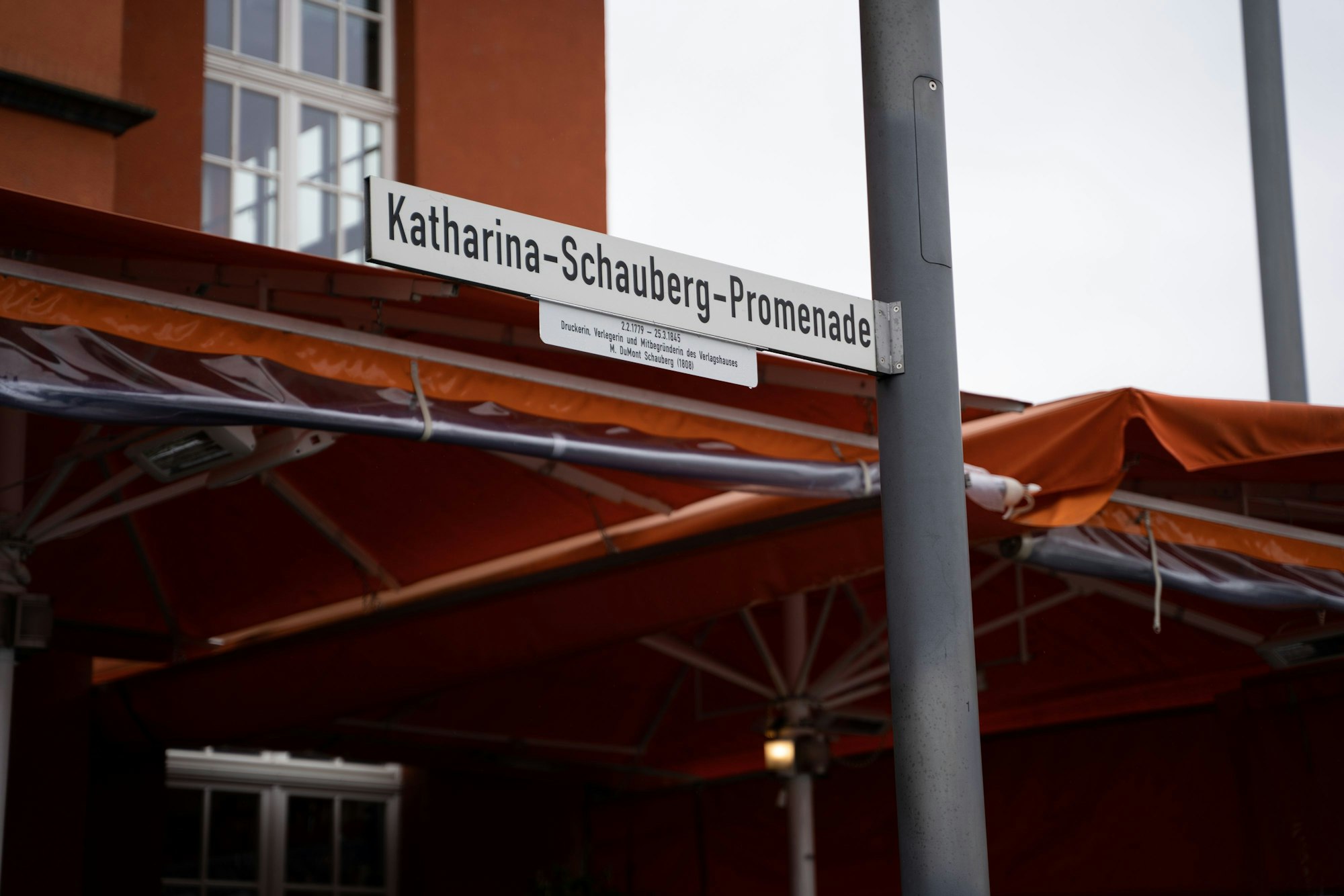 Das Straßenschild der Katharina-Schauberg-Promenade samt Ergänzungstafel am Rheinauhafen.