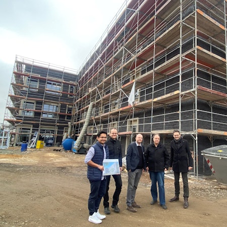 Fünf männliche Personen vor einem Gebäude, das ein Baugerüst um sich hat