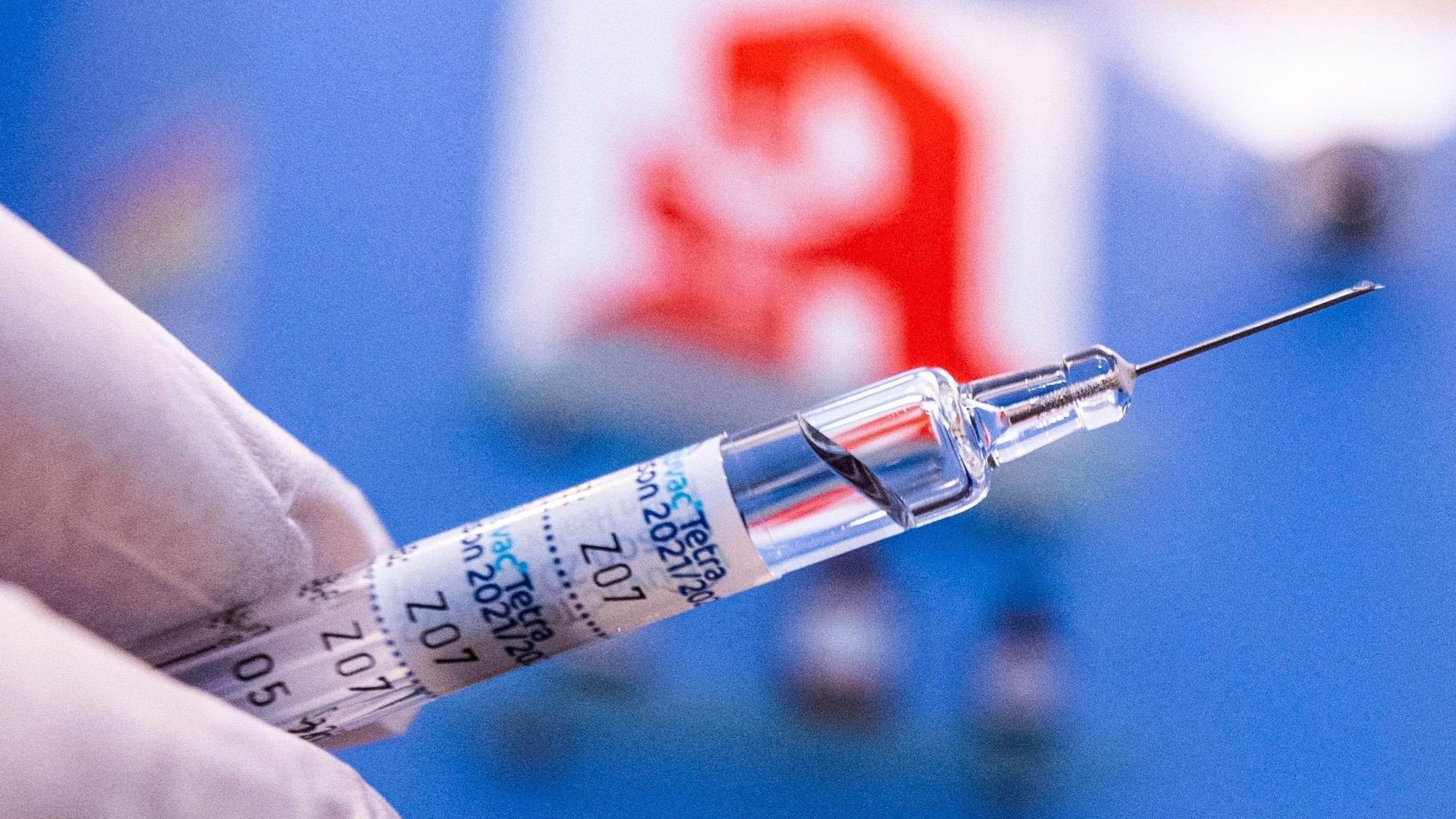 Dieses Symbolfoto zeigt, wie ein Apotheker eine Spritze mit Grippeschutzimpfstoff vor dem Logo der Apotheke in der Hand hält.