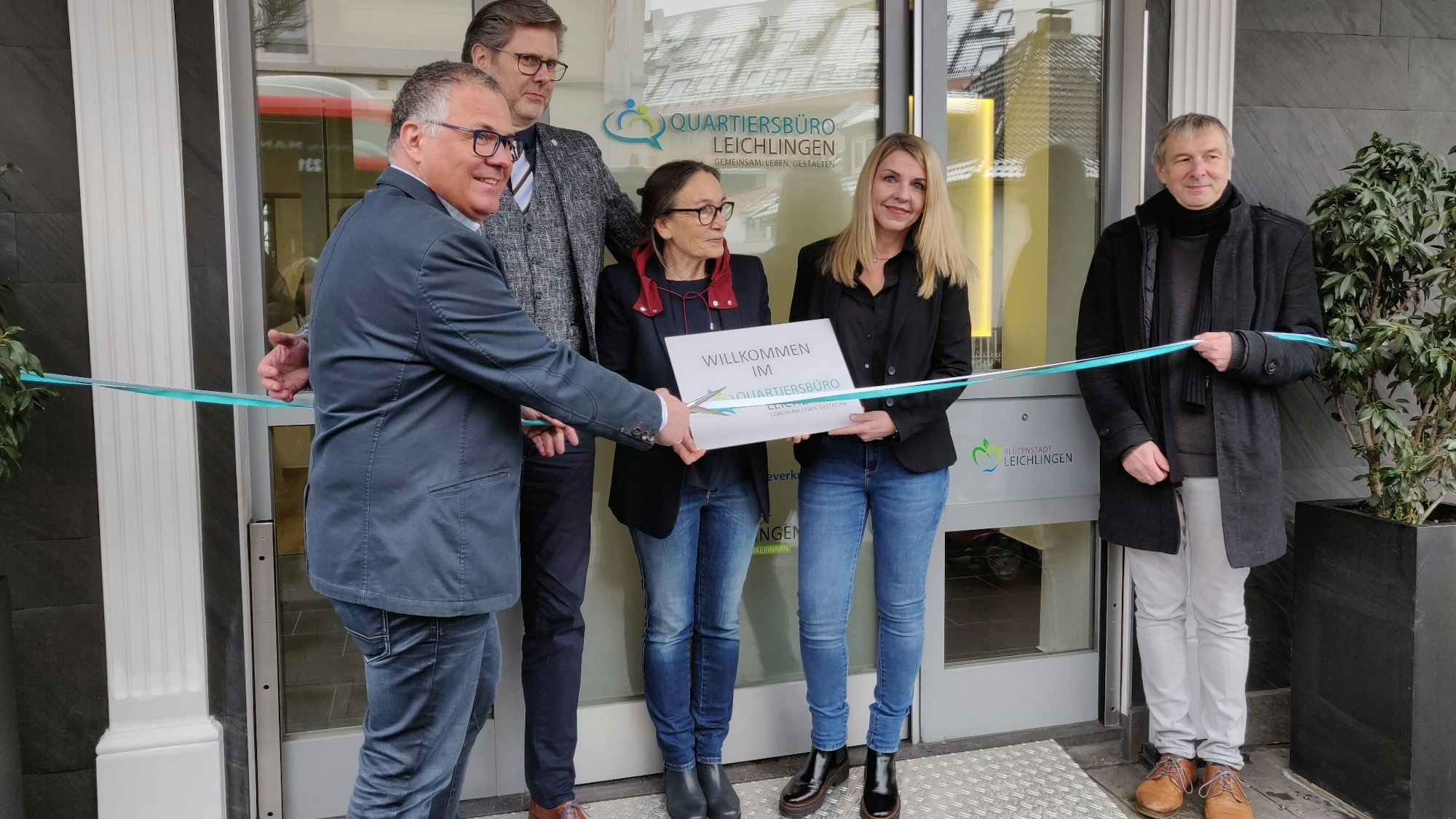 Bürgermeister Frank Steffes mit Schere am Eröffnungsband vor der Türe des Quartiersbüros mit Superintendent Bernd-Ekkehart Scholzen, Romana Arendes und Aleksandra Petz vom Sozialamt und Thomas Holtzmann vom Diakonischen Werk.