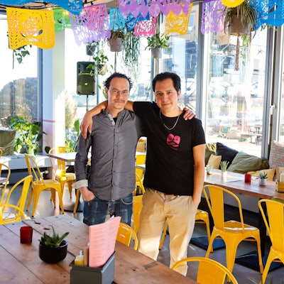 zwei Männer stehen Arm in Arm zwischen Tischen und Stühlen in einem Restaurant