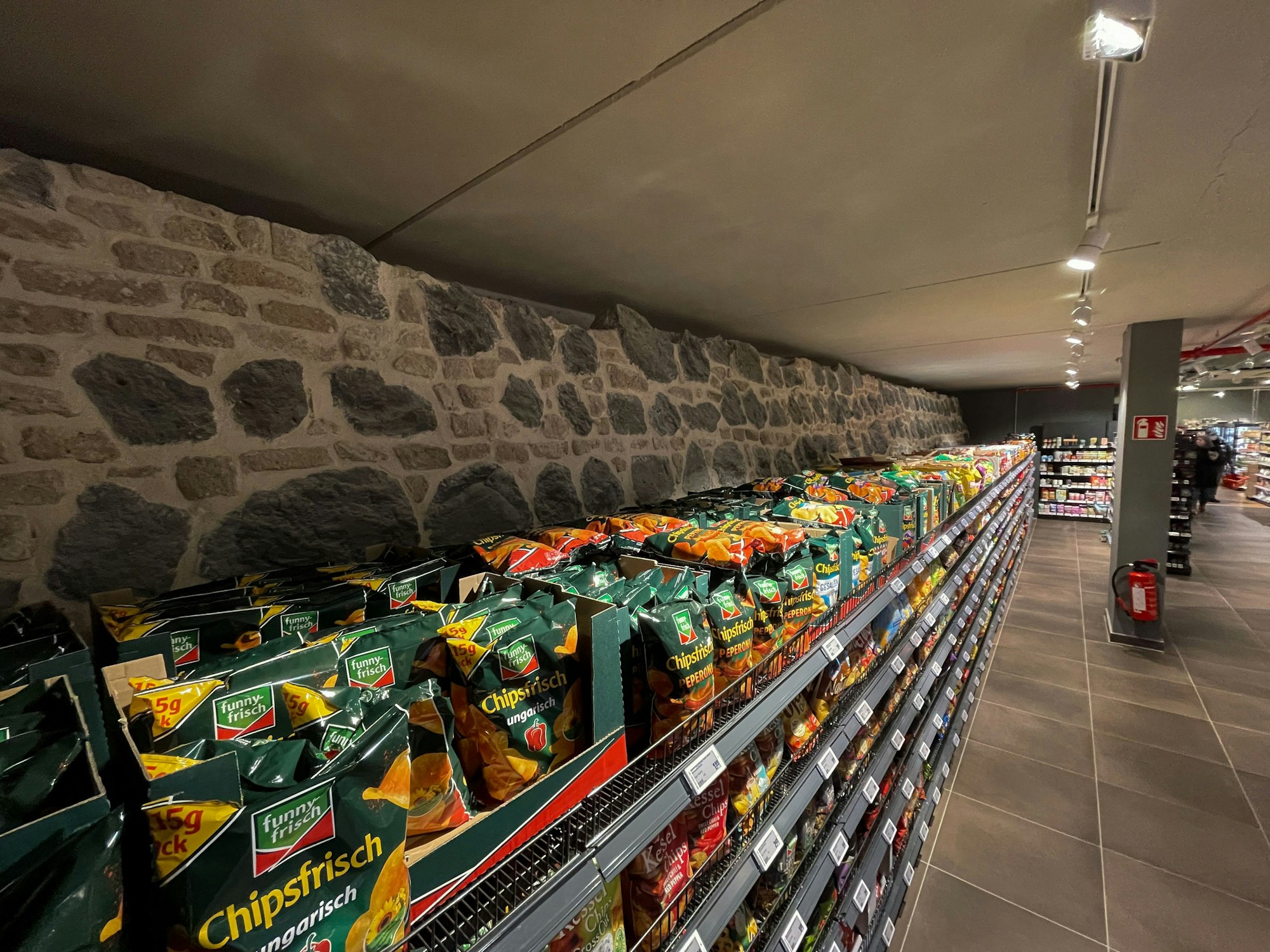 Ein Regal mit Chips, dahinter ein rund 15 Meter langes Stück der Stadtmauer.