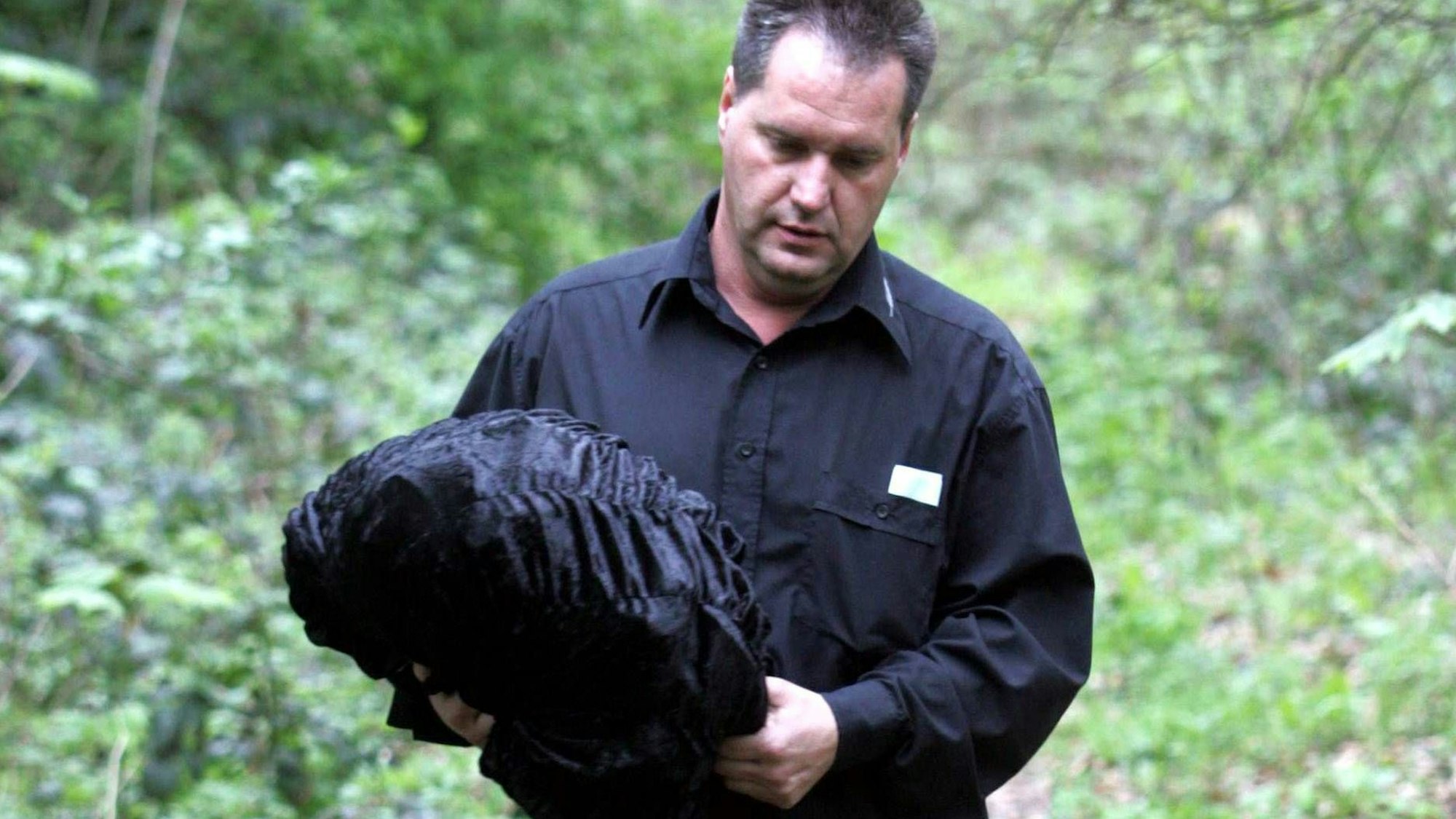 Ein Bestatter trägt ein schwarzes Bündel.