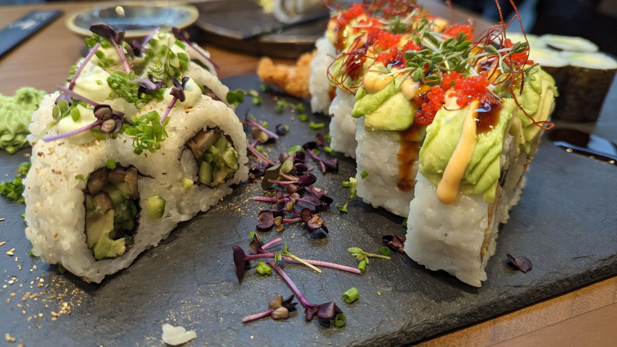 Verzierte Sushi-Rollen mit Reis stehen auf einer schwarzen Schieferplatte.